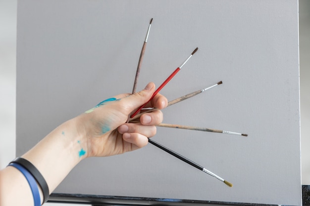 The girl artist holds different brushes for painting with oil paints on clean canvas.