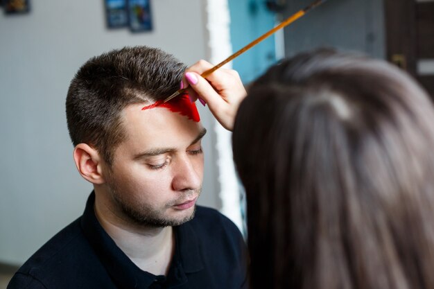 Girl artist paints on a man’s face