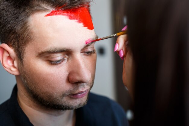 Girl artist paints on a man’s face