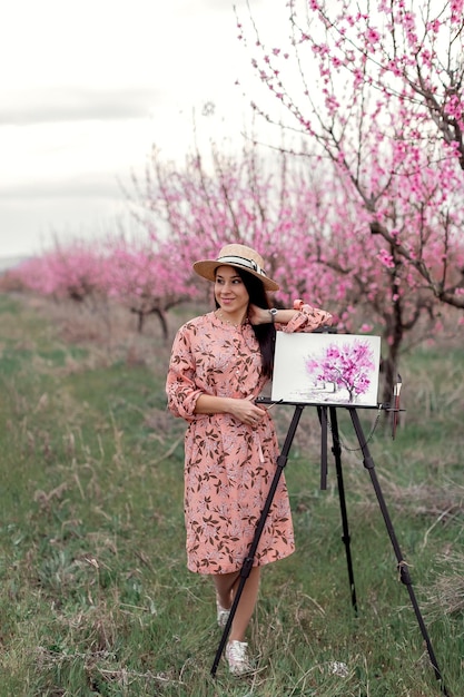 Girl artist paints a peach orchard in a peach orchard spring