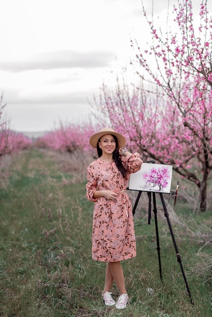 Foto l'artista della ragazza dipinge un frutteto di pesche in una primavera di frutteto di pesche