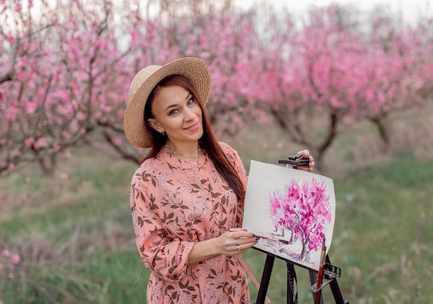 Girl artist paints a peach orchard in a peach orchard spring