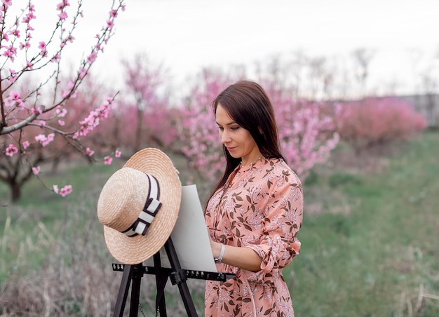 少女芸術家が桃の果樹園の春に桃の果樹園を描く
