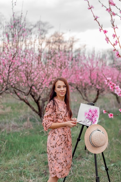 Girl artist paints a peach orchard in a peach orchard spring