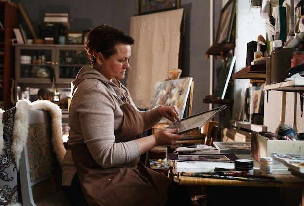 A girl artist in the studio inserts a picture into a frame