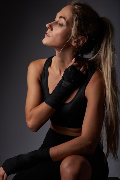 Girl athlete in black sportswear with bandages on her arms resting after training