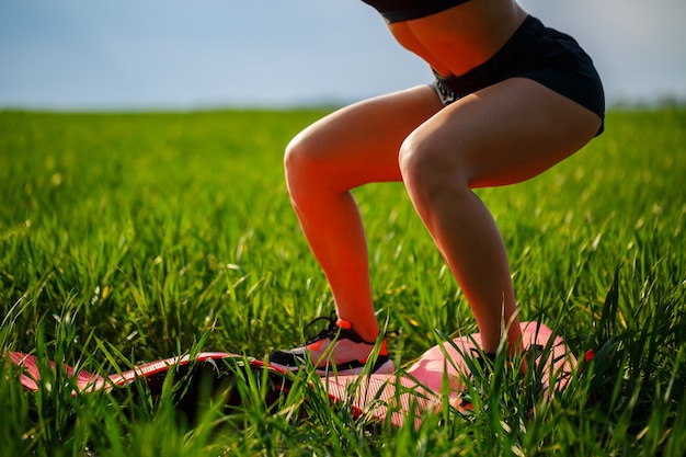 Foto l'atleta della ragazza fa squat in natura, esercizi per i glutei. la giovane donna pratica sport, stile di vita sano, corpo atletico. indossa abbigliamento sportivo, top nero e pantaloncini.