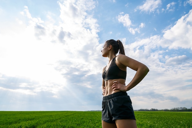 女子アスリートは屋外でウォームアップ、筋肉のエクササイズをします。若い女性は、スポーツ、健康的なライフスタイル、運動体のために行きます。彼女はスポーツウェア、黒のトップス、ショートパンツを着ています。スポーツのコンセプト。