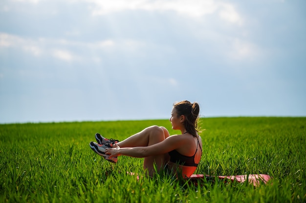 Girl athlete shakes the press lies on a rug in nature. Young woman go in for sports, healthy lifestyle, athletic body.