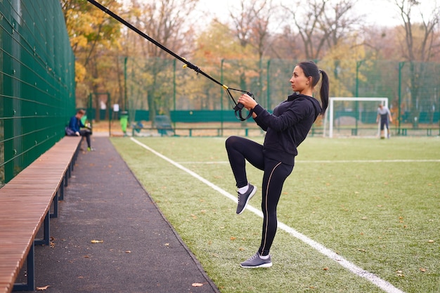 Девушка-спортсменка тренируется с использованием trx на спортивной площадке