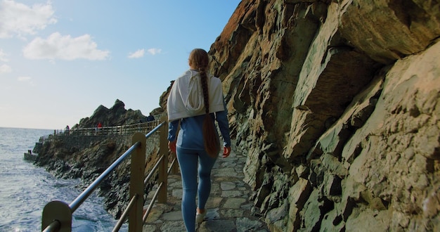 Girl athlete walks in a tracksuit along the promenade waterfront at sunrise Rear view of woman injoying ocean waves Tenerife Canary islands Slow motion