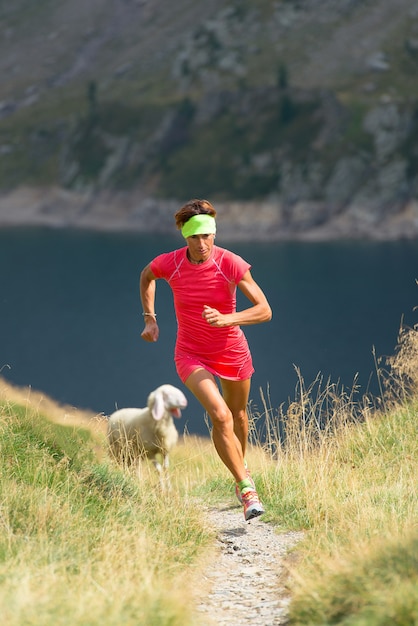 Girl athleterun in a mountain path with sheep near