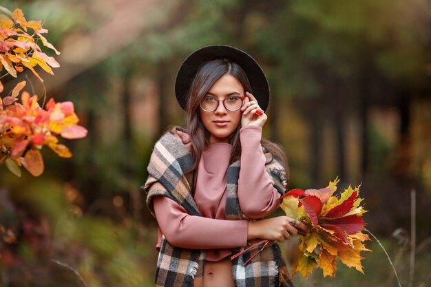 Ragazza nella foresta di autunno con un mazzo di foglie di autunno