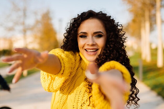 A girl in an autumn park in a bright yellow sweater gleefully smiling drags her hands forward with her fingers melted like a child39s