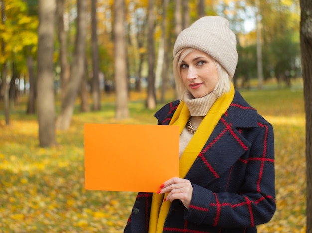 Una ragazza in un parco autunnale tiene un pezzo di carta per il tuo testo. libretto pubblicitario