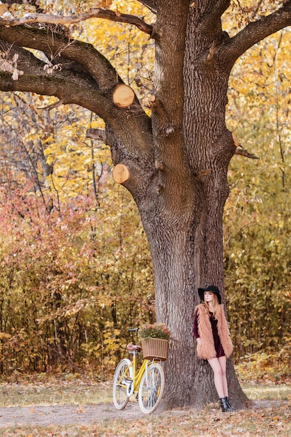 黄色の自転車で散歩の女の子秋は木の下に立つ