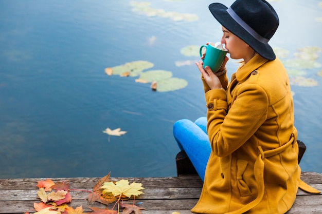 Girl in the autumn the water Heats about a Cup of hot tea