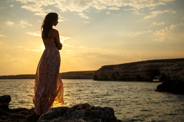 美しい海の景色と夕日、崖の上、美しい空と海の上の少女のシルエットの背景の上の少女