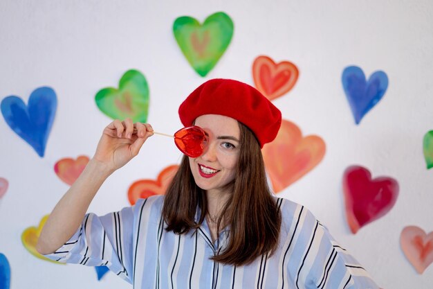 A girl on a background of colorful bright hearts with a red lollipop heart smiles closing her eye the concept of valentine's day love