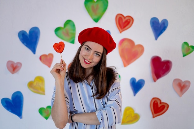 A girl on the background of colorful bright hearts with a red lollipop heart smiles the concept of valentine's day love