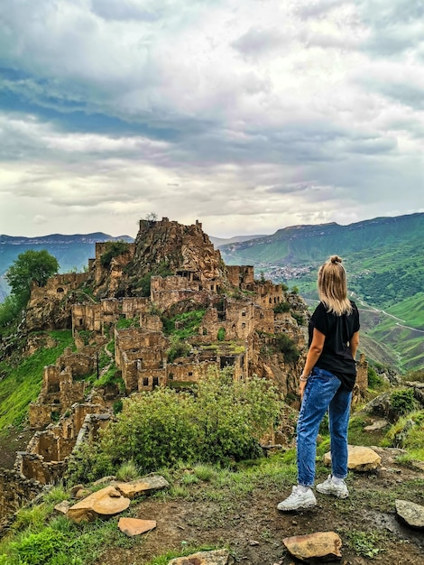 A girl on the background of Gamsutl village in the Caucasus mountains on top of a cliff Dagestan Russia June 2021