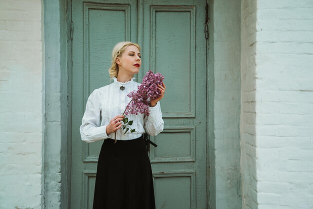 Girl on the background of a gray door with a branch of lilac