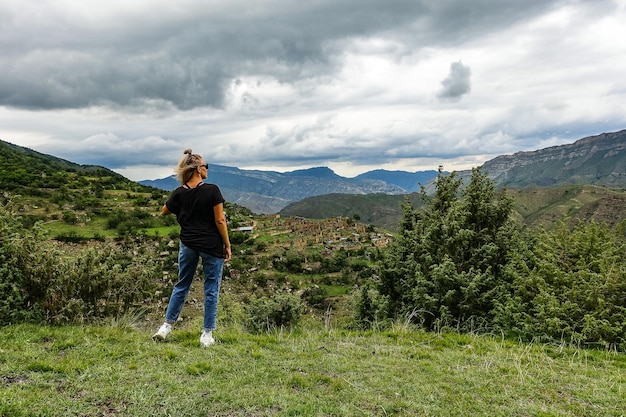 崖の上にあるコーカサス山脈のクリブ村の背景にいる少女ダゲスタンロシア2021年6月