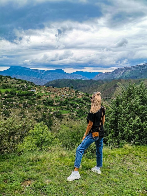 A girl on the background of the village of Kurib in the Caucasus mountains on top of a cliff Dagestan Russia June 2021