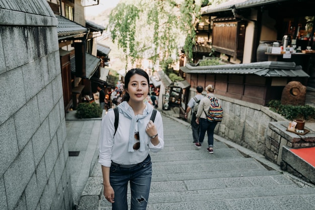 girl backpacker smiling climbing walking up stairs in sannen zaka street. many foreign tourists visit famous attraction kyoto japan. beautiful woman traveler cheerful visiting japanese style old town