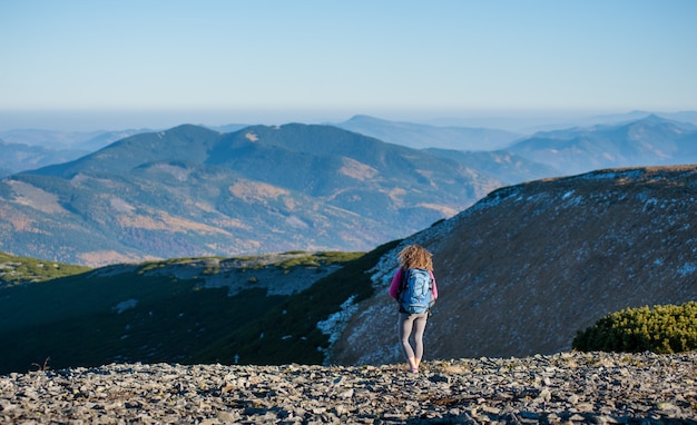 Girl backpacker standing on the ridge of the mountain enjoying the open view on the big mountains