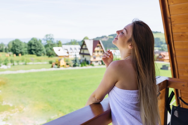 Girl on the balcony in a white towel holding a cup of coffee