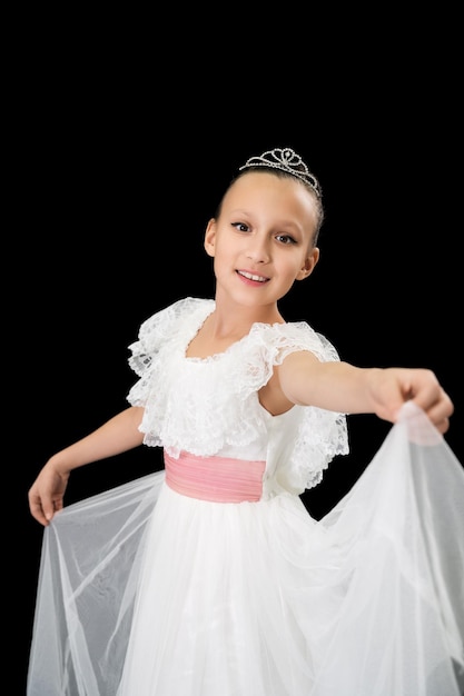 Girl ballet dancer with diadem on head dressed in white long dress dancing on black background