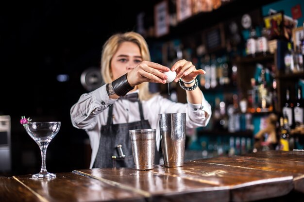 Девушка-бармен готовит коктейль в баре