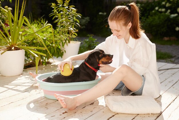 한 소녀 가 정원 의 샤워실 에서 푸 를 사용 하여 개 를 목욕 시킨다