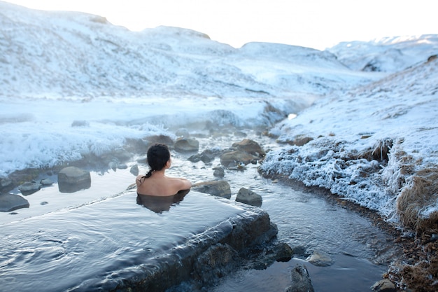 Девушка купается в горячем источнике на открытом воздухе с великолепным видом на снежные горы. Невероятная Исландия зимой