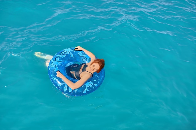 Girl in a bathing suit is resting on sea on inflatable ring young redhaired woman floats on ocean in...