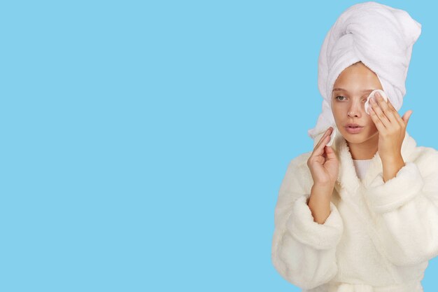 A girl in a Bathrobe cleanses her skin with cotton pads after a shower on an isolated