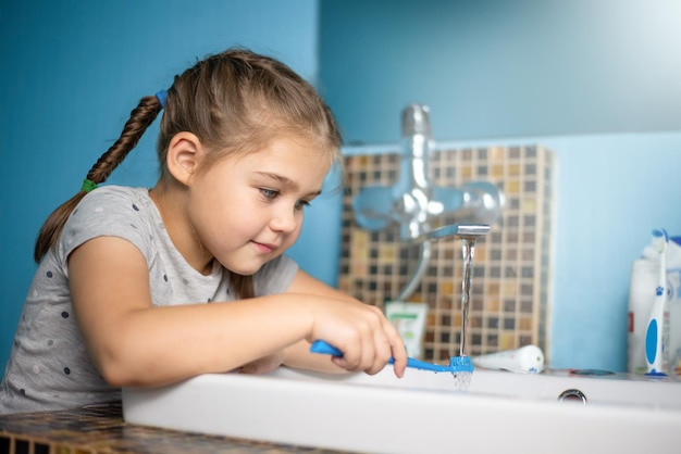 Photo girl in the bathroom washes a toothbrush under water