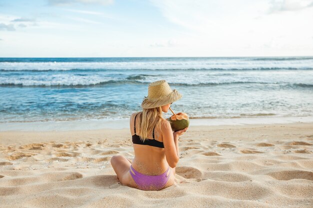 Girl on the beach drinking a young coconut, back view