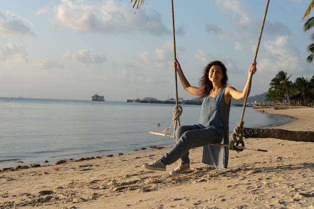 girl on the beach rides on a swing during sunset