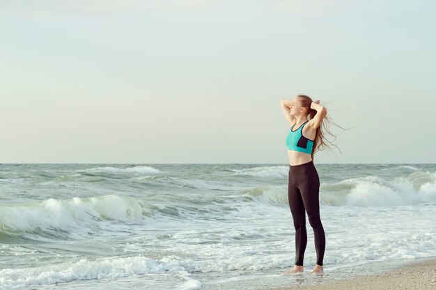 Girl on the beach standing with hands behind head. Morning sun