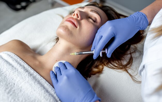 girl beautician makes injections on the lips and face of a beautiful woman in a cosmetic wedge. cosmetology concept.
