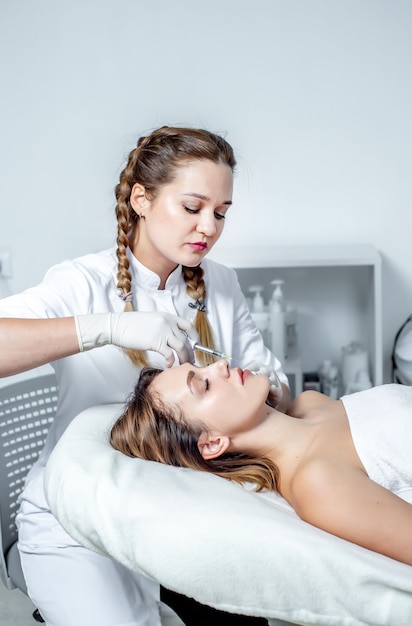 girl beautician makes injections on the lips and face of a beautiful woman in a cosmetic wedge. cosmetology concept.