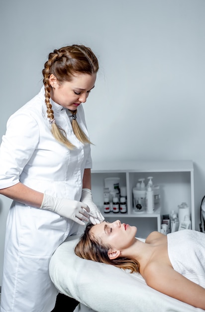 L'estetista della ragazza fa le iniezioni sulle labbra e sul viso di una bella donna in un cuneo cosmetico. concetto di cosmetologia.