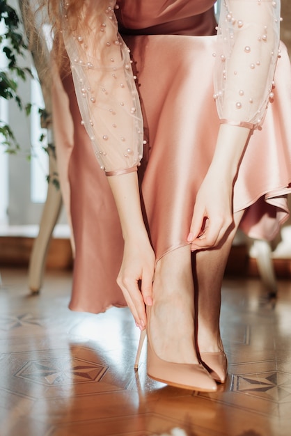 Girl in a beautiful dress puts on beige shoes on her feet