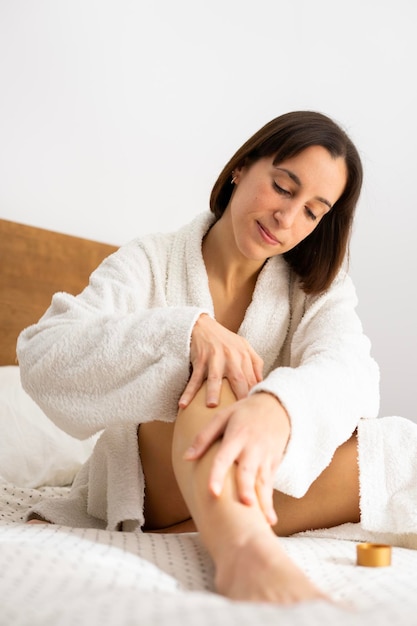 Girl in bed in bathrobe putting cream on her legs after shower