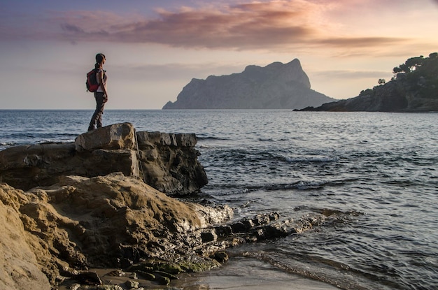 Девушка смотрит на море со скалы на закате