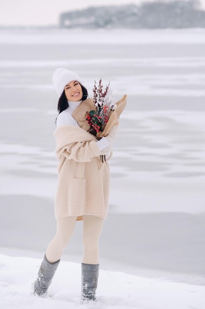 A girl in a beige cardigan and winter flowers walks in nature\
in the snowy season winter weather