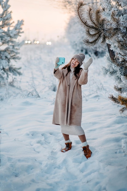 a girl in a beige faux fur coat tooks selfie in a snowy forest beautiful fairy winter in the forest