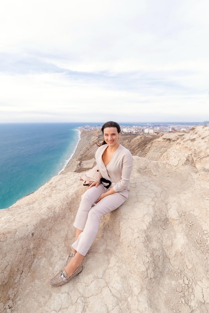 a girl in beige is sitting on a rock against the background of the sea